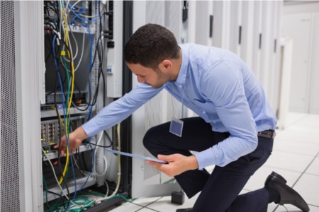 Man checking tablet pc as he is plugging cables into server in data center